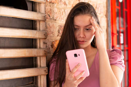 Woman with worried expression while looking at her cell phone.の写真素材