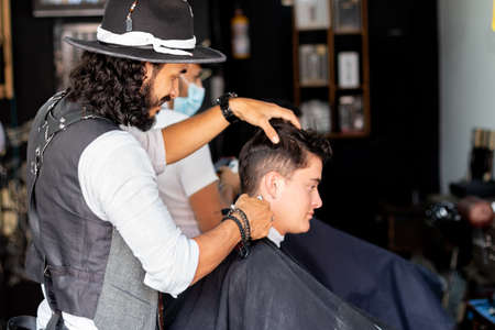 Stylish barber with hat cutting hair of a young client.の写真素材