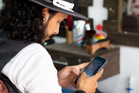 Stylist sitting in his barbershop chair using his smartの写真素材