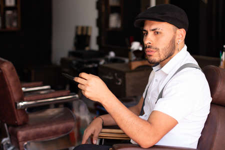 Barber playing with the scissors in his hands sitting in his barbershop chair. Man with cap.の写真素材