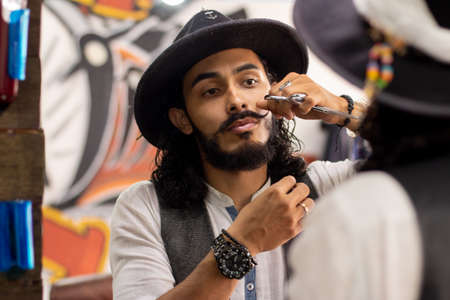 Hipster grooming his mustache in front of the mirror. Man wearing hat and elegant watch.の写真素材