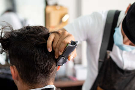 Barber with face mask using hair clipper on client. Stylist cutting hairの写真素材