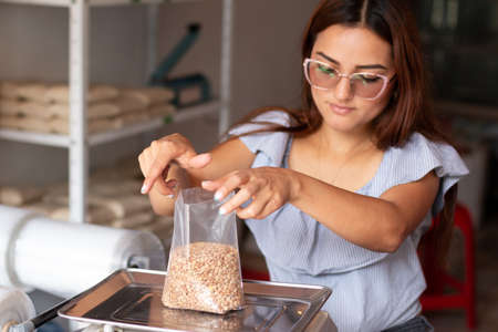 Focused womans hands packing grains in transparent bag to sell. Lentils and grain store.の写真素材
