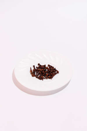Cloves for cooking on a white background. Stack of nails on small plate. Medicinal plant.