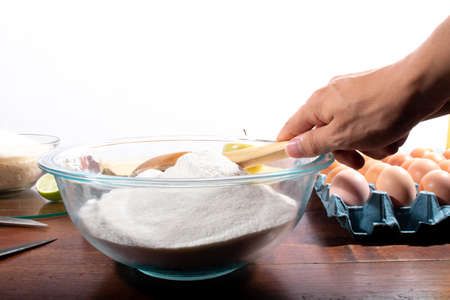 Hand pouring flour into a bowl with a wooden spoon. Using wooden spoon to pour wheat flour into...