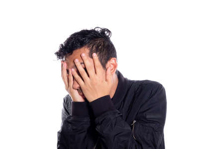 Embarrassed man covering his face with his hands. White background. Man covering his face and looking at camera through fingers.の写真素材
