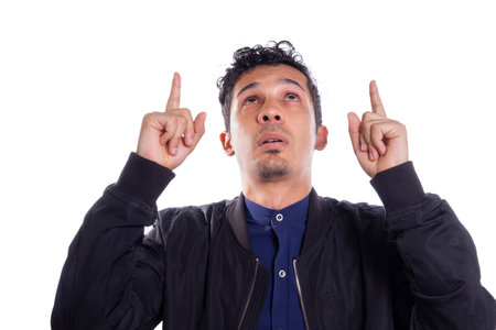 Man pointing up with both hands, white background. Young adult Latino young man looking up.