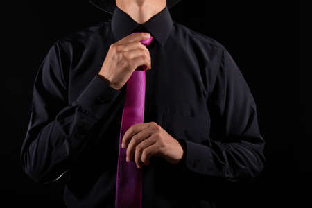 Elegant man tying his tie over black shirt. Adjusting tie. Black and violet. Young business man dressing, isolated on black background. Groom adjusting his tie.の写真素材