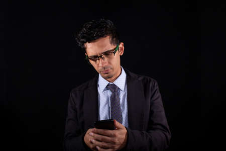 Business man looking at his smart phone, isolated on black background. Young adult business man...