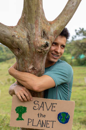 Man asks save the planet. Young adult latin man holds sign asking to save the planet while hugging a...