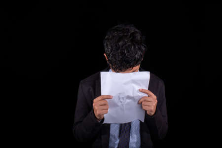 Young businessman crying over a document and covering his face, isolated on black background.の写真素材