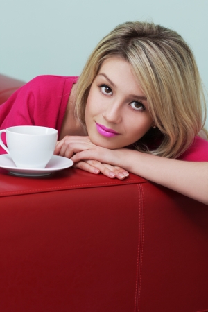 Blonde sits on the couch with a cup of coffee の写真素材