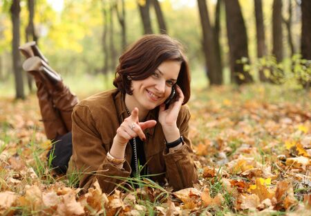 woman calling by phone in autumn park の写真素材