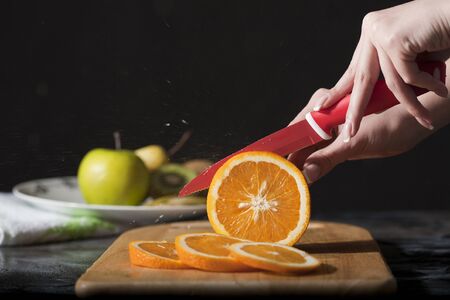 Woman's hands cutting fresh orange on kitchenの写真素材