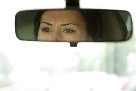 Young woman sits on driver's seat and Looks in the rear-view mirror の写真素材
