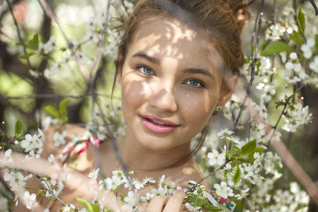 Portrait of Beautiful young woman standing near blooming trees in spring garden の写真素材