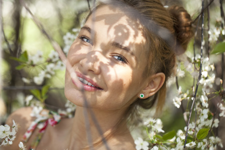 Portrait of Beautiful young woman standing near blooming trees in spring garden の写真素材