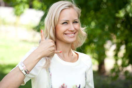 Portrait of attractive young woman on open air. Woman making a call me sign outdoors の写真素材