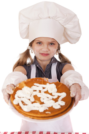 Beautiful happy seven year old girl in chef uniform with shortcakes and whipped cream, studio on white backgroundの写真素材
