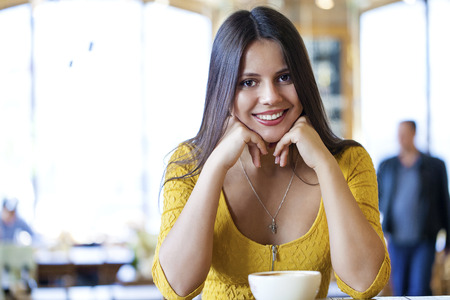 Beautiful young brunette woman sitting in a coffee shop and drink teaの写真素材