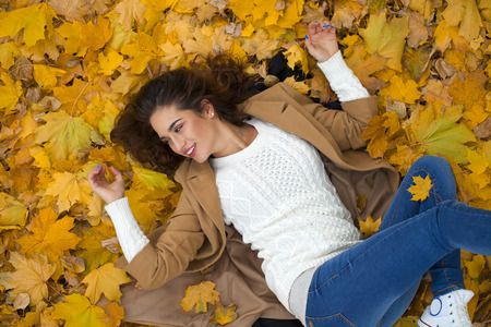 Young beautiful girl in blue jeans lying on yellow leaves, view from above, in the autumn parkの写真素材