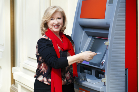 Mature blonde woman with credit card in hand near automated teller machine in shopの写真素材
