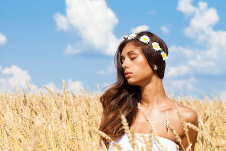 Beautiful young woman in white dress on wheat golden fieldの写真素材