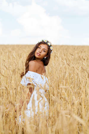 Beautiful young woman in white dress on wheat golden fieldの写真素材