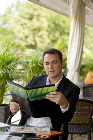 Young Businessman holding a menu sitting in a summer restaurantの写真素材