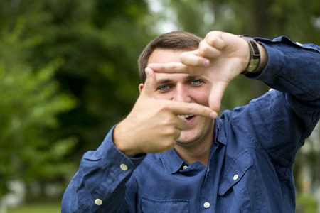 A man looking and focusing through his hands, on green summer backgroundの写真素材