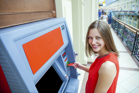 Young happy brunette woman withdrawing money from credit card at ATMの写真素材