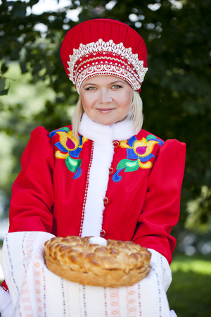Young woman is dressed in the Russian national dress. She holds in his hands the fresh loaf. It is a custom to meet the guests.の写真素材