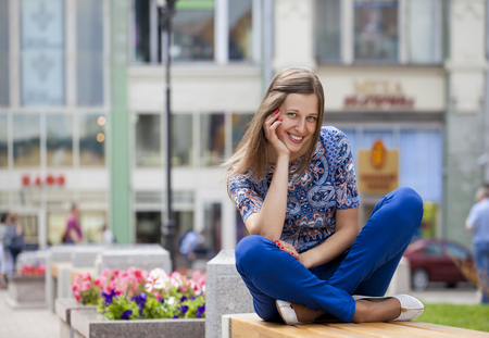 Happy Beautiful young woman sits on a bench in a summer streetの写真素材