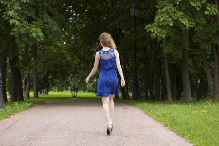 Portrait in full growth, attractive young blonde woman in blue dress walking in summer parkの写真素材