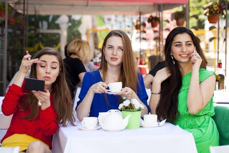 Three young beautiful girls girlfriend drinking tea in a summer cafe