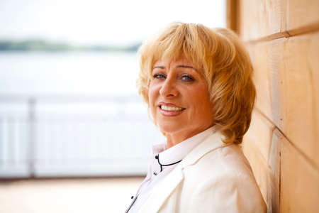 Happy elderly woman in a white jacket on the background of wooden wallの写真素材