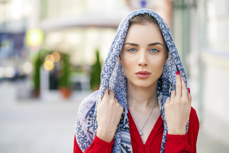 Beautiful young brunette woman in a blue scarf on summer street city