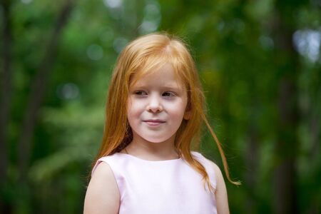 Portrait of a little red-haired girl on the background of summer green forestの写真素材