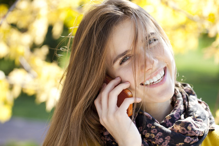 Happy beautiful woman calling by phone in autumn streetの写真素材