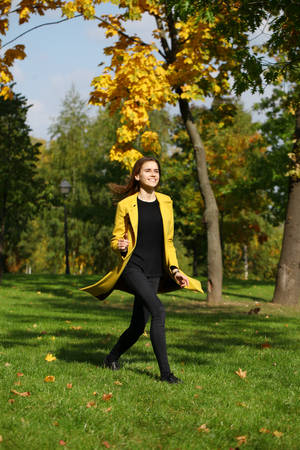 Beautiful woman in yellow coat walking autumn streetの写真素材