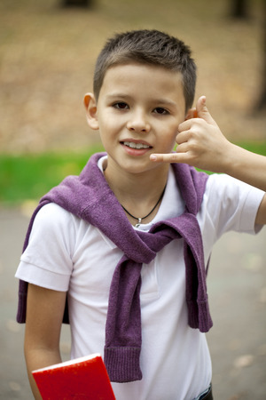 Little Boy making a call me gesture, against background of summer parkの写真素材
