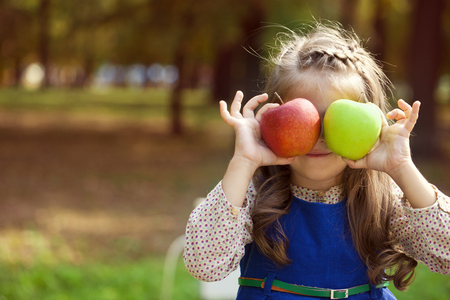 Portrait of a little girl with two large apples on a background of autumn parkの写真素材