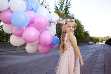 Little five-year girl in a pink dress holding balloons, against background of summer streetの写真素材