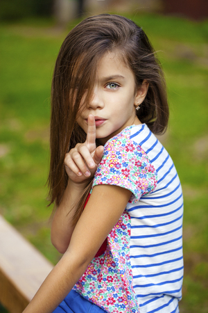 Young beautiful Little girl has put forefinger to lips as sign of silence, outdoors summerの写真素材