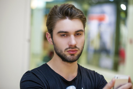 Young handsome man in a black knitted sweater photographing themselves on a cell phoneの写真素材