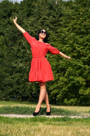 Beautiful young woman in red dress walking in summer parkの写真素材