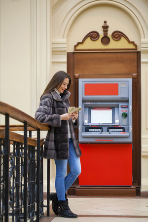 Woman hand showing dollar banknotes in front of the red atmの写真素材