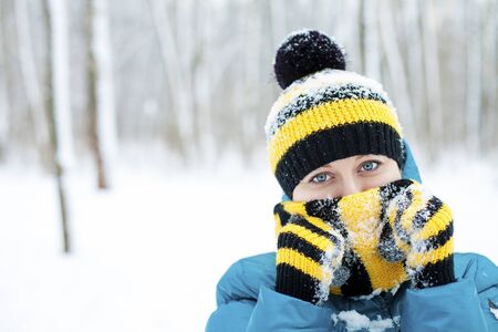 Portrait of a beautiful young woman in a turquoise feather bed and a knitted cap on a background of a winter parkの写真素材
