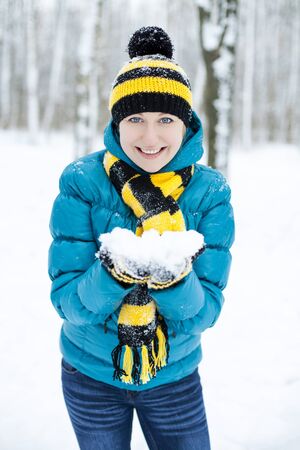 Portrait of a beautiful young woman in a turquoise feather bed and a knitted cap on a background of a winter parkの写真素材