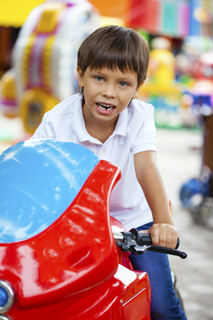 Little boy sitting on a toy red motorcycle in an amusement parkの写真素材